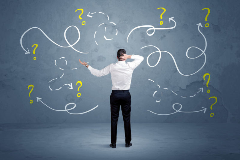 Unsure businessman with question marks A salesman in doubt can not find the solution to the problem concept with curvy lined arrows and question marks drawn on urban wall