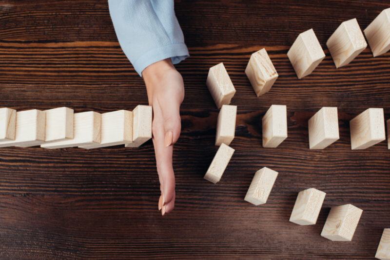 cropped view of woman preventing wooden blocks from falling at desk